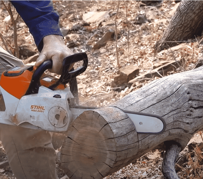 operating an electric chainsaw on a log