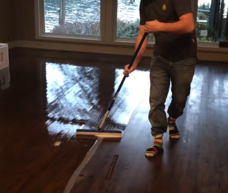 person applying polyurethane varnish on hardwood floor
